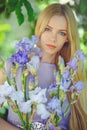 Attractive young girl with blonde dren hair and natural make-up smelling blue purple iris flowers on a background outdoors, tender Royalty Free Stock Photo