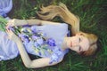 Attractive young girl with blonde dren hair and natural make-up smelling blue purple iris flowers lying on grass outdoors, tendern Royalty Free Stock Photo