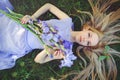 Atraktivní mladý blondýnka vlasy a přírodní vonící modrý purpurová kosatec květiny ležící na tráva venku 
