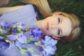 Attractive young girl with blonde dren hair and natural make-up smelling blue purple iris flowers lying on grass outdoors, tendern Royalty Free Stock Photo