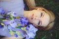 Attractive young girl with blonde dren hair and natural make-up smelling blue purple iris flowers lying on grass outdoors, tendern Royalty Free Stock Photo