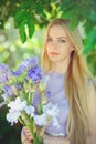 Attractive young girl with blonde hair and natural make-up smelling blue purple iris flowers on a background outdoors, tender Royalty Free Stock Photo