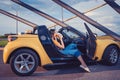 Young girl in blue jeans, orange top and flip flops is eating hamburger while sitting in yellow car cabrio. Fast food