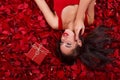 Attractive girl lies in rose petals near a gift box and holds hand near the face. Royalty Free Stock Photo