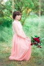 Attractive young girl in a long dress, with a bouquet of burgundy peonies in her hands on a swing in a summer park Royalty Free Stock Photo