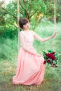 Attractive young girl in a long dress, with a bouquet of burgundy peonies in her hands on a swing in a summer park Royalty Free Stock Photo