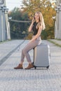 Attractive young girl is phoning sitting on the suitcase on the bridge