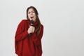 Attractive young girl in red winter sweater with long brown hair holding microphone with both hands and singing out loud