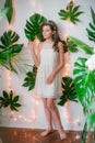 Attractive young girl in a romantic white dress among tropical greenery and white orchids, roses and lilies.