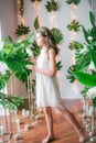 Attractive young girl in a romantic white dress among tropical greenery and white orchids, roses and lilies.