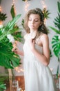 Attractive young girl in a romantic white dress among tropical greenery and white orchids, roses and lilies.