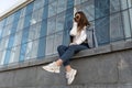 Attractive young girl in sunglesses in youth clothing on the summer street. Stylish young woman resting on city street