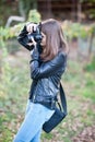 Attractive young girl taking pictures outdoors. Cute teenage girl in blue jeans and black leather jacket taking photos in park Royalty Free Stock Photo