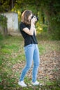 Attractive young girl taking pictures outdoors. Cute teenage girl in blue jeans and black t-shirt taking photos in autumnal park. Royalty Free Stock Photo