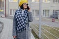 An attractive young girl wearing sunglasses in a coat walking down the street and talking on the phone and smiles Royalty Free Stock Photo