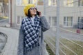 An attractive young girl wearing sunglasses in a coat walking down the street and talking on the phone and smiles Royalty Free Stock Photo