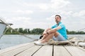 Attractive young guy sits in blue polo on pier near the yacht. smiled tourist handsome man relaxing and enjoying the view on pier Royalty Free Stock Photo