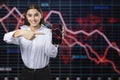 Attractive happy caucasian businesswoman pointing at cellphone with glowing downward red forex chart on blurry background.