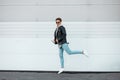 Attractive young hipster man in black glasses in a fashionable leather black jacket in a light pink sweatshirt in blue jeans Royalty Free Stock Photo