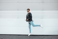 Attractive young hipster man in black glasses in a fashionable leather black jacket in a light pink sweatshirt in blue jeans in Royalty Free Stock Photo