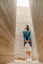 Attractive young woman stands between concrete walls. Caucasian girl in casual jeans and flower dress looks up. Royalty Free Stock Photo