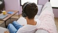 Attractive young hispanic man immerses in heart-touching song, chilling out on sofa at home, lost in melody through high-tech Royalty Free Stock Photo