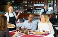 Hispanic waitress serving pizza to friendly company in restaurant