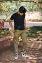 Attractive young indian man full height portrait in black t shirt, silver neck chain in green park Royalty Free Stock Photo