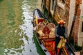 Attractive young Italian Gondolier wearing straw hat stands in traditional gondola with luxury decor