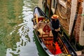 Attractive young Italian Gondolier wearing straw hat stands in traditional gondola with luxury decor