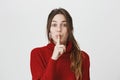 Attractive young lady with long brown hair wearing fashinable red sweater holding her index finger near mouth over white Royalty Free Stock Photo