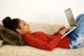 Attractive young lady lying on sofa typing on laptop