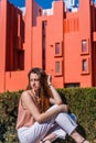 Attractive young lady sitting on a patio in front of geometric red buildings