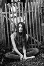 Attractive young long-haired woman in jeans sits near a wooden fence. Royalty Free Stock Photo