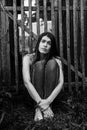 Attractive young long-haired woman in jeans sits near a wooden fence. Royalty Free Stock Photo