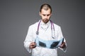 Attractive young male doctor looking to the camera seriously while examining an x-ray scan of his patient posing on grey backgroun Royalty Free Stock Photo