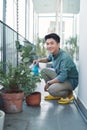 Attractive Young Man on Apartment Balcony Watering Plants in Box from Blue Watering Can