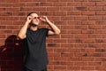 Attractive young man in black t-shirt standing near the red brick wall holding sunglasses with his hands Royalty Free Stock Photo