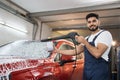 Attractive young man, car wash worker is spraying cleaning foam to a modern red luxury car Royalty Free Stock Photo