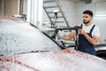 Attractive young man, car wash worker is spraying cleaning foam to a modern red luxury car Royalty Free Stock Photo