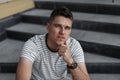 Attractive young man in a fashionable striped t-shirt with a stylish hairstyle posing while sitting on stone vintage steps Royalty Free Stock Photo