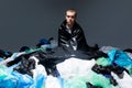 Attractive young man with haircut seated and covered with plastic bag garbage, dark light background