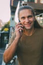 Attractive young man hipster talking on a smartphone while sitting on the steps of a glass business center. Urban fast life