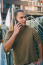 Attractive young man hipster talking on a smartphone while sitting on the steps of a glass business center. Urban fast life