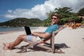 Attractive young man with laptop working on the beach. Freedom, remote work, freelancer, technology, internet, travel and vacation Royalty Free Stock Photo