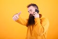 Attractive young man with long beard talking on the phone and showing thumbs up sign over yellow background
