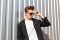 Attractive young man model in a fashionable black shirt in a t-shirt straightens stylish sunglasses. European hipster guy Royalty Free Stock Photo