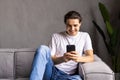 Attractive young man sitting on a floor in the living room, using mobile phone Royalty Free Stock Photo