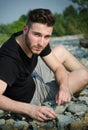 Attractive young man sitting on rock and pebbles