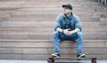 Attractive young man sitting on wooden steps in an urban city park with his skating board, Royalty Free Stock Photo